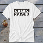 White t-shirt with black text reading "CREEK RAISED" in a box.