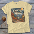 Yellow t-shirt graphic with text "Took the long way home for October" and autumn mountain scene.