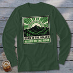 Dark green long-sleeve t-shirt with a graphic of mountains, sun rays, and text reading Born in the Holler Raised on the Ridge.