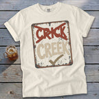 Cream t-shirt with a distressed sign graphic reading "CRICK" crossed out and "CREEK" with a checkmark.