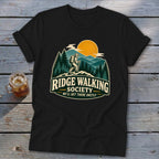 Black t-shirt with "Ridge Walking Society" logo featuring a hiker, mountains, trees, and sun.