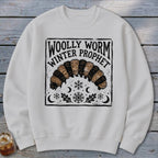 White crewneck sweatshirt featuring a black graphic of a woolly worm, snowflakes, and the text Woolly Worm Winter Prophet.