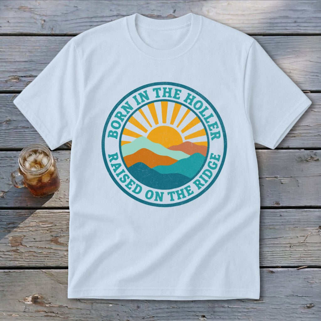 A white t-shirt featuring a retro mountain graphic with the text Born in the Holler Raised on the Ridge.