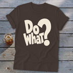 A dark brown crewneck t-shirt with rolled-up sleeves, featuring the white text "Do what?" on the chest, laid flat on a rustic wooden surface next to a glass of iced tea.