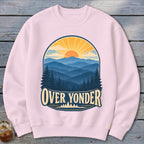 Light pink crewneck sweatshirt featuring a graphic of mountains, trees, and a setting sun with text reading OVER YONDER.