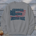 Gray crewneck sweatshirt featuring a distressed American flag graphic and text reading Georgia Raised American Made.