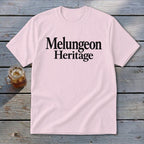 A light pink short-sleeve t-shirt with the black text Melungeon Heritage displayed on the chest.