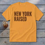 Orange t-shirt with brown text "NEW YORK RAISED" and a glass of iced drink.