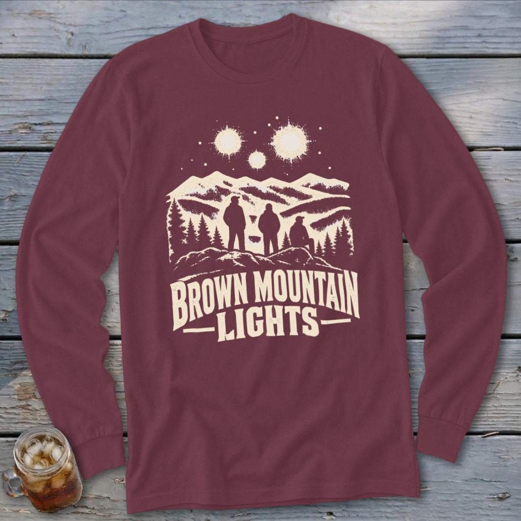 Maroon long-sleeve t-shirt featuring a graphic of three figures, mountains, glowing orbs, and text reading Brown Mountain Lights.