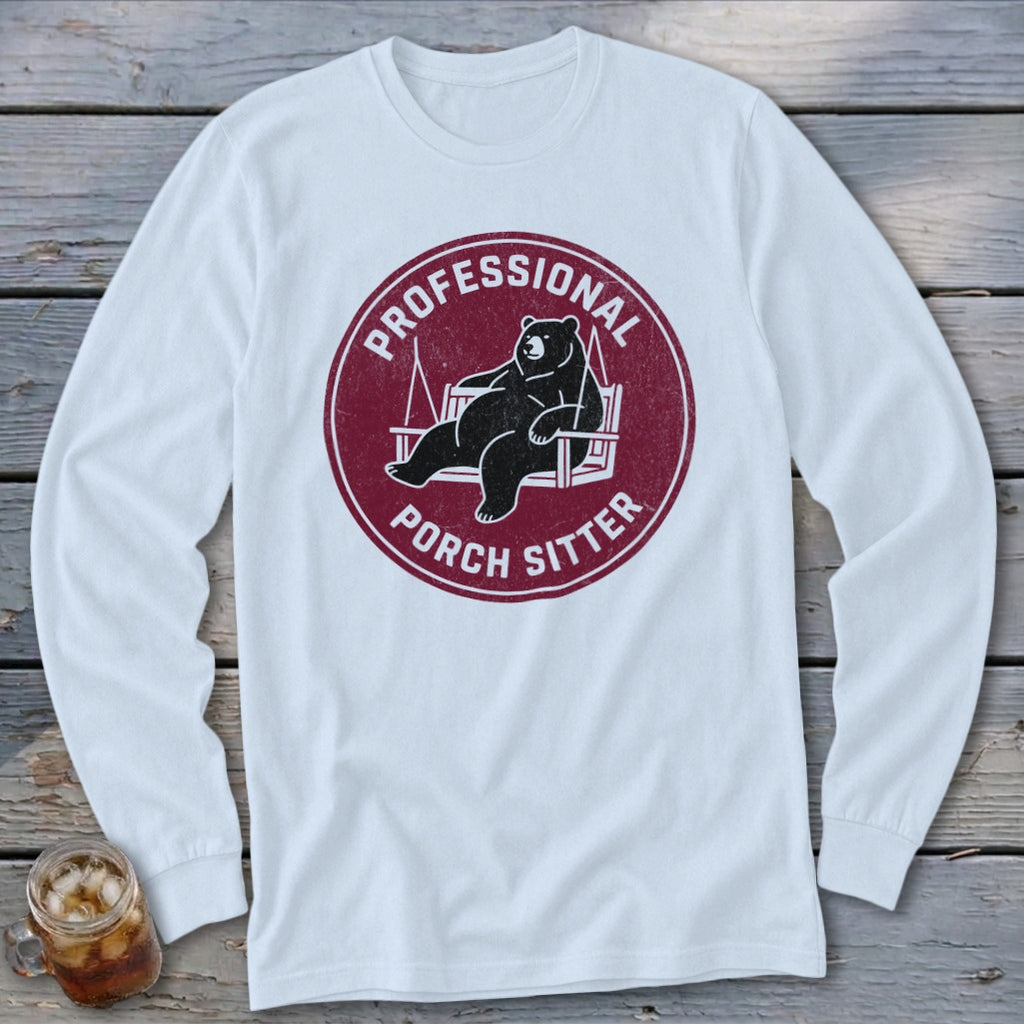 White long-sleeve t-shirt with a maroon circular graphic of a bear lounging on a porch swing, labeled PROFESSIONAL PORCH SITTER.