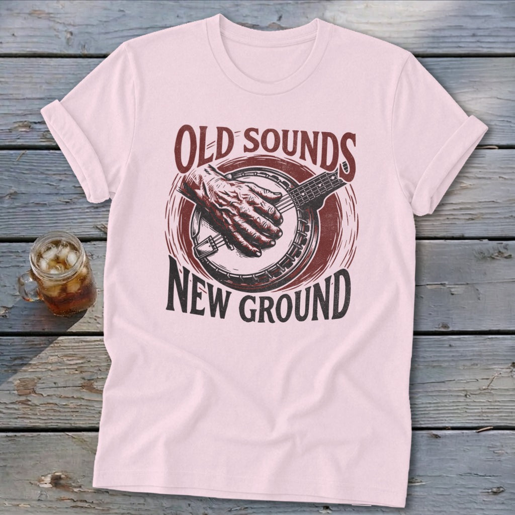 Light pink t-shirt featuring a red banjo graphic and the text OLD SOUNDS NEW GROUND.