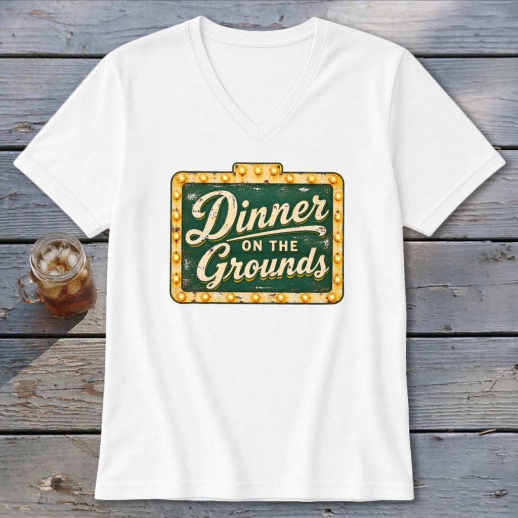 A white V-neck t-shirt featuring a green vintage-style marquee sign graphic that reads Dinner on the Grounds.
