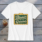 A white V-neck t-shirt featuring a green vintage-style marquee sign graphic that reads Dinner on the Grounds.