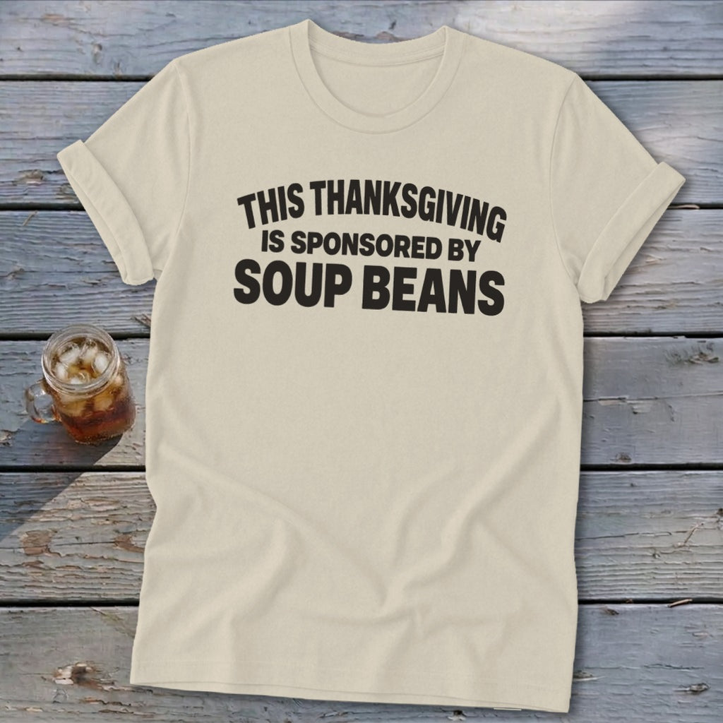 Cream t-shirt with rolled sleeves featuring bold black text that reads, THIS THANKSGIVING IS SPONSORED BY SOUP BEANS.