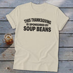 Cream t-shirt with rolled sleeves featuring bold black text that reads, THIS THANKSGIVING IS SPONSORED BY SOUP BEANS.