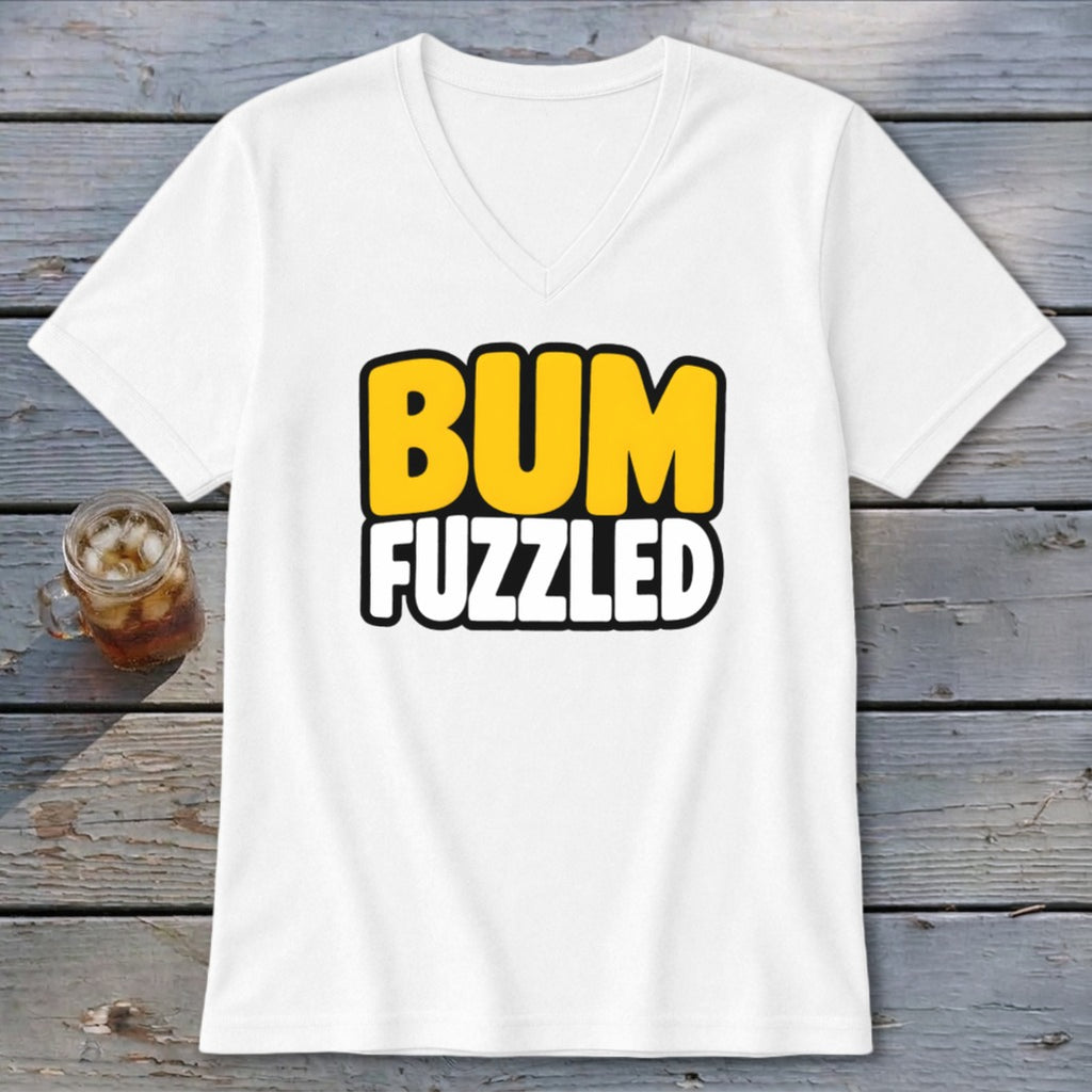 A white V-neck t-shirt with the text BUM FUZZLED on the front rests on a wooden surface next to a glass of iced tea.