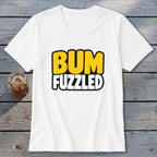 A white V-neck t-shirt with the text BUM FUZZLED on the front rests on a wooden surface next to a glass of iced tea.