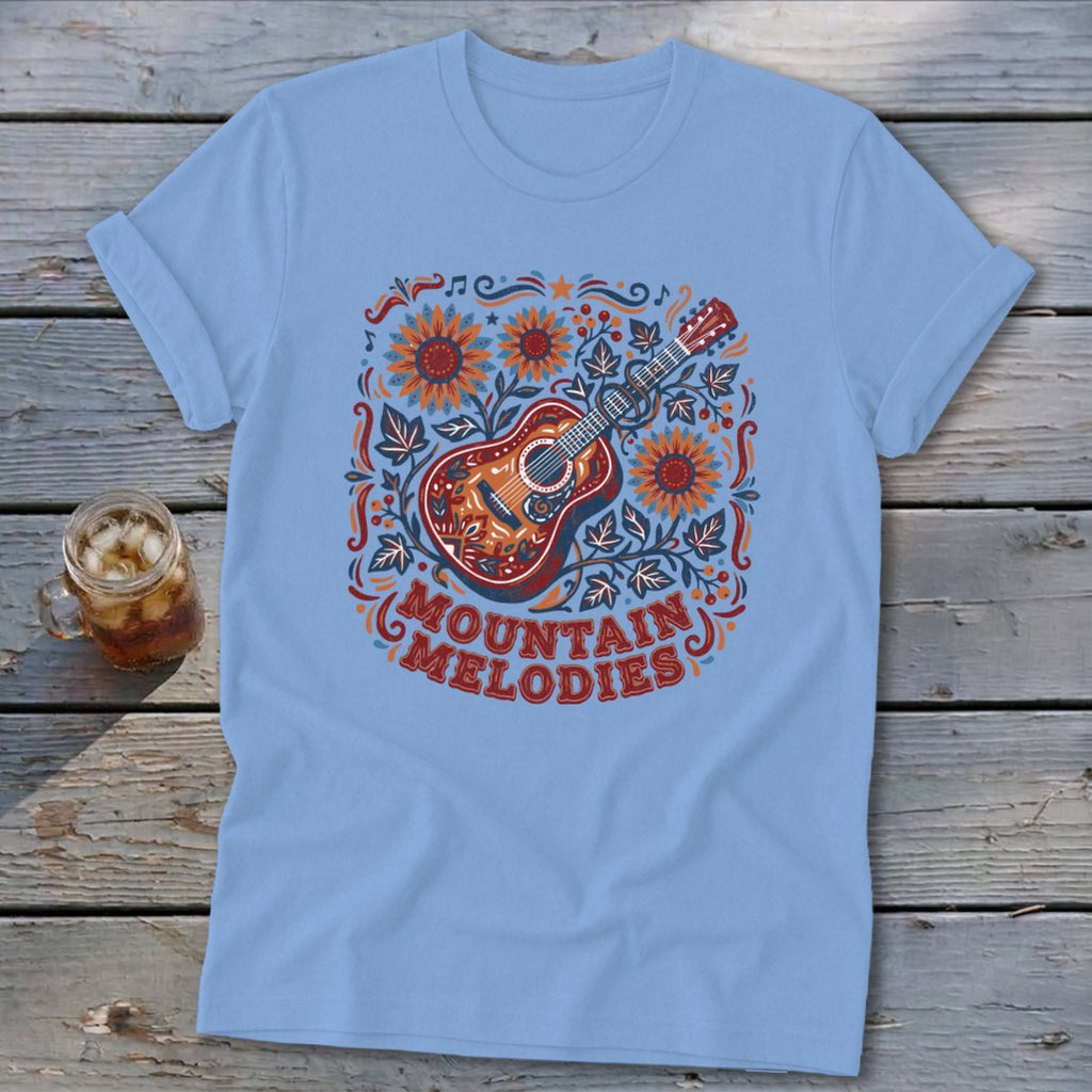 Light blue t-shirt featuring a folk-art graphic of a guitar, sunflowers, and the text MOUNTAIN MELODIES.