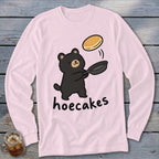 Light pink long-sleeved t-shirt featuring a cartoon black bear flipping a pancake in a pan, with the text hoecakes.