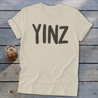 Light beige t-shirt with "YINZ" printed in dark gray on the front.