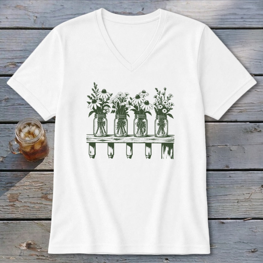 A white V-neck t-shirt featuring a green graphic of four mason jars filled with wildflowers on a shelf.