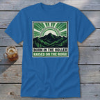 A blue t-shirt featuring a green mountain graphic with text that reads Born in the Holler Raised on the Ridge.