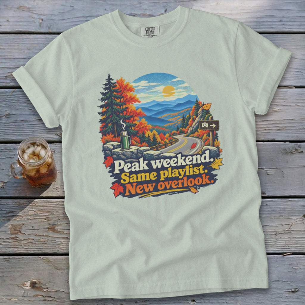 T-shirt with fall mountain road graphic and text "Peak weekend. Same playlist. New overlook."
