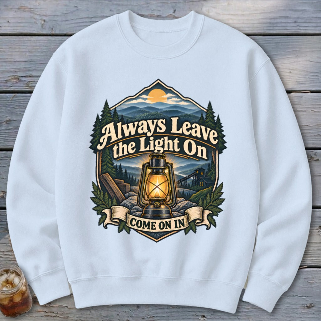 White sweatshirt with vintage lantern, mountains, trees, and text "Always Leave the Light On Come On In".