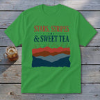 A green t-shirt featuring the text "Stars, Stripes & Sweet Tea" and a layered mountain landscape graphic.
