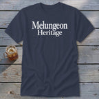 Dark blue crewneck t-shirt featuring the white text Melungeon Heritage, displayed on a wooden surface beside a glass jar of iced tea.