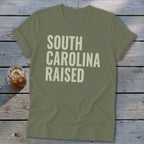 Olive green t-shirt with "SOUTH CAROLINA RAISED" printed in light green text.