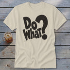 A cream-colored crewneck t-shirt lies flat on a wooden surface, featuring black bold text that reads "Do What?".