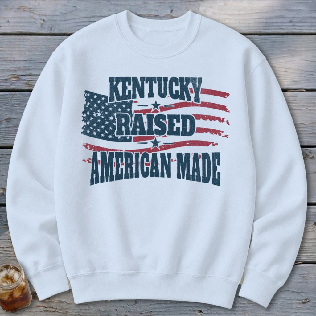 White sweatshirt with distressed American flag graphic reading "Kentucky Raised American Made."