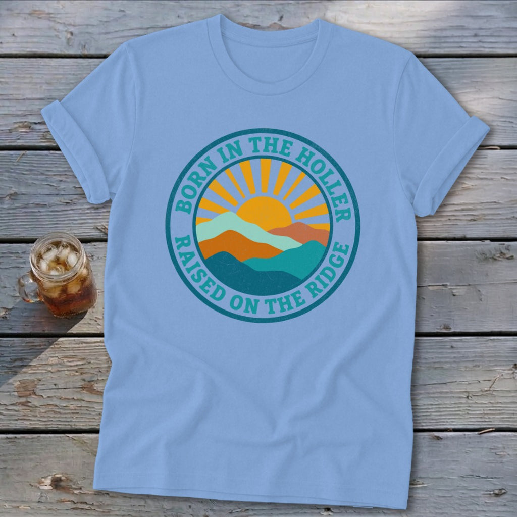 Light blue t-shirt featuring a retro mountain and sun graphic with the text Born in the Holler Raised on the Ridge.