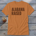 Orange t-shirt with "ALABAMA RAISED" in dark brown text.
