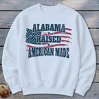 White sweatshirt with distressed "Alabama Raised American Made" text and US flag design.