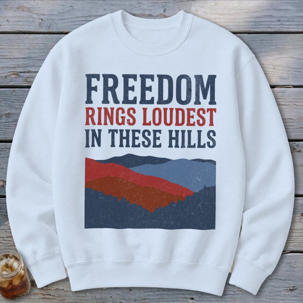 A white crewneck sweatshirt featuring a graphic of rolling hills and red, white, and blue text.