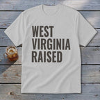 White t-shirt with "WEST VIRGINIA RAISED" printed in dark gray block letters.