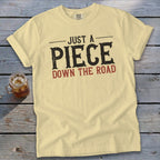 Light yellow t-shirt with "JUST A PIECE DOWN THE ROAD" graphic.