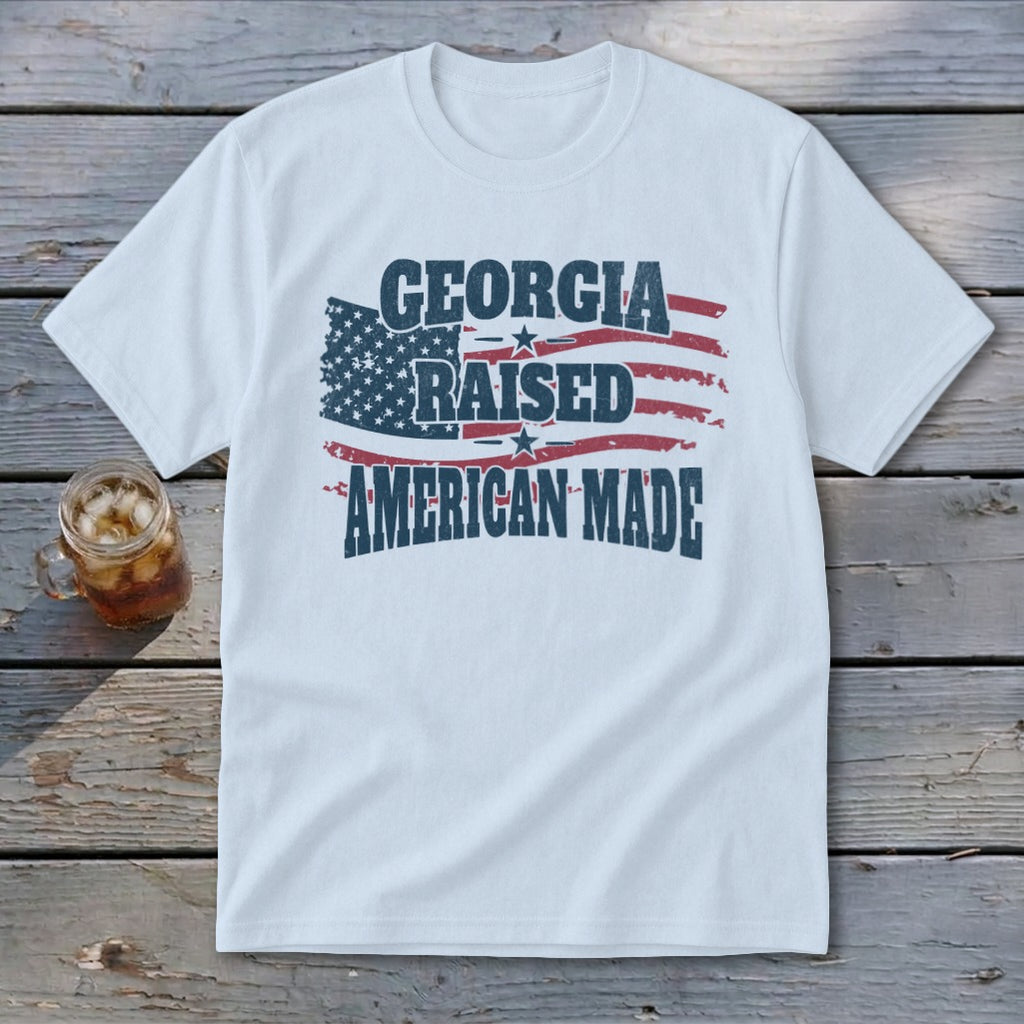 White crewneck t-shirt with distressed text reading GEORGIA RAISED AMERICAN MADE over a wavy American flag.