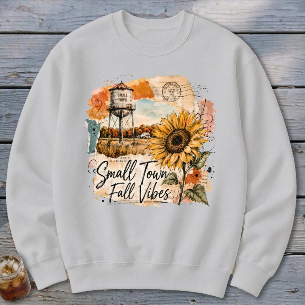 White sweatshirt with "Small Town Fall Vibes" graphic featuring a sunflower and water tower.