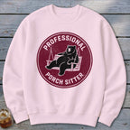 Light pink crewneck sweatshirt featuring a maroon circular graphic of a bear relaxing on a porch swing, with the text Professional Porch Sitter.