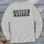 White long-sleeve shirt with black text reading "CREEK RAISED"