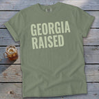 Olive green t-shirt with "GEORGIA RAISED" printed in light yellow text.