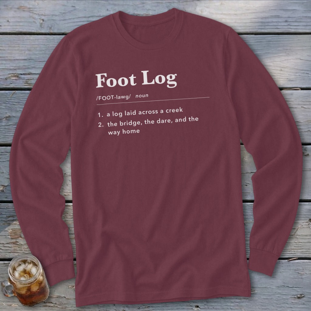 Maroon long-sleeve t-shirt with white dictionary-style text defining Foot Log laid across a wooden background.