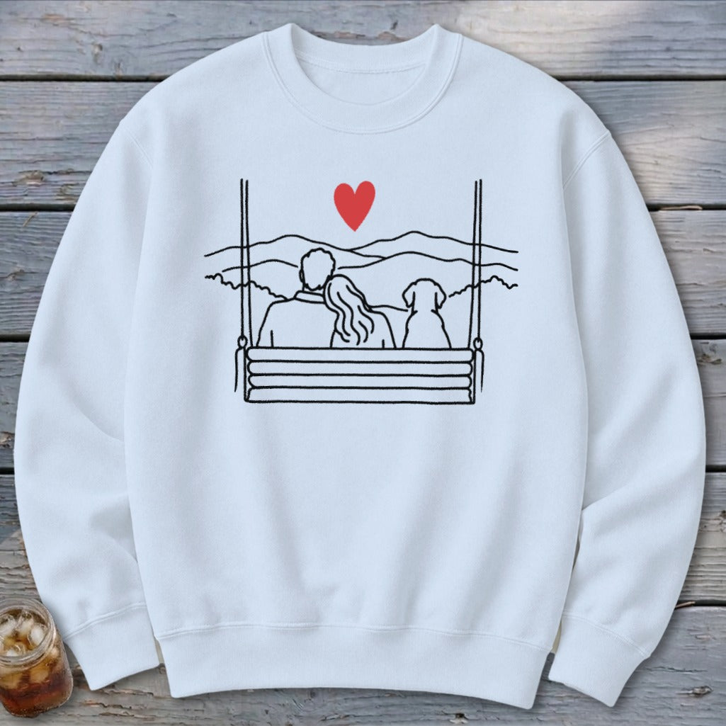 Sweatshirt with line drawing of couple and dog on a swing overlooking mountains and a red heart.