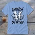 Light blue t-shirt graphic with text "Barefoot on the Creek Bank" and bare feet in water.