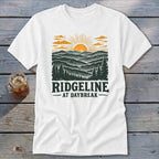 White t-shirt with "RIDGELINE AT DAYBREAK" text and mountain sunrise graphic.