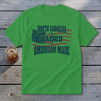 Green t-shirt with distressed American flag graphic and text reading North Carolina Raised American Made.