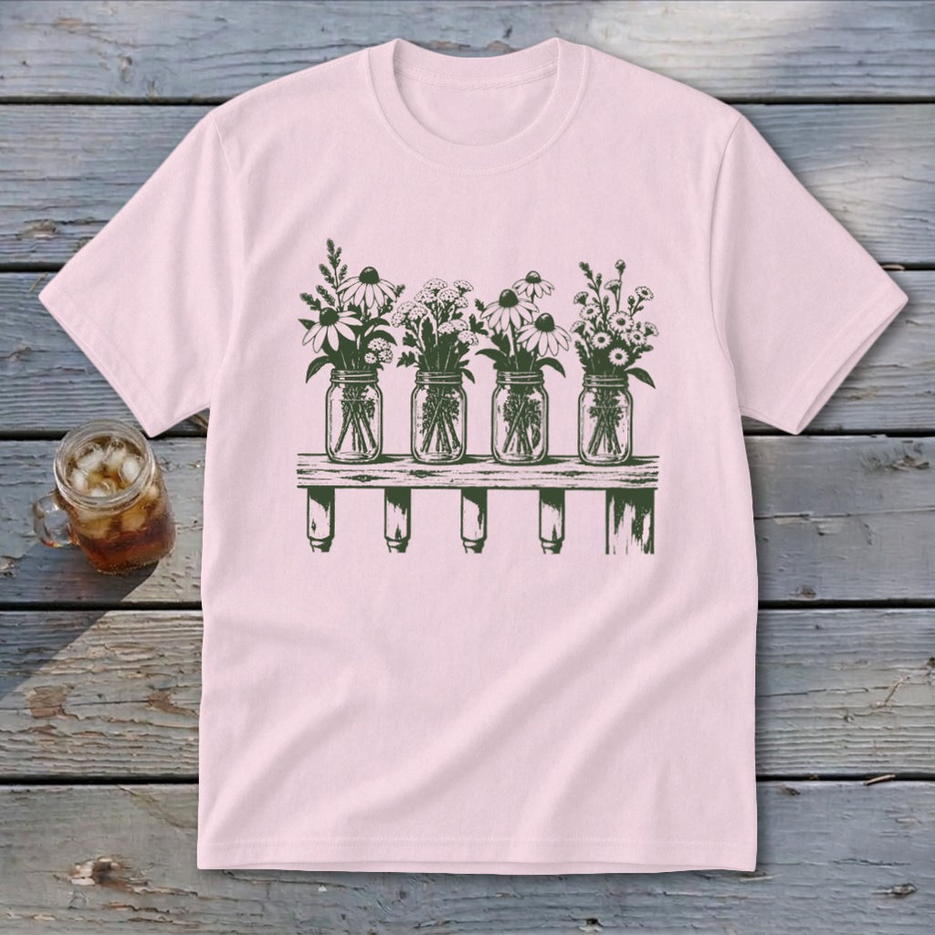 A light pink t-shirt featuring a green graphic of four mason jars filled with wildflowers on a shelf.